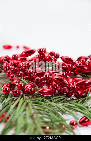 Perline rosse lucide nei rami di pino isolate su sfondo bianco. Decorazioni. Natale, Capodanno, compleanno, festa. Verticale. Copia spazio Foto Stock