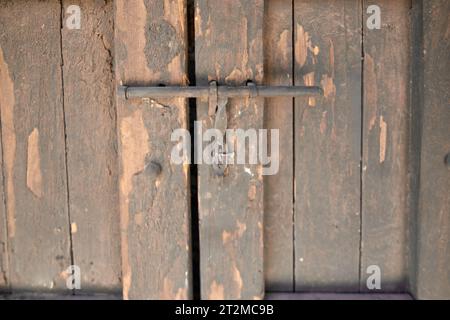 Porta vecchia in tavole di legno verticali con vernice per spellatura. Il dispositivo di chiusura è una semplice barra metallica con un gancio su un'estremità La porta è chiusa e la chiusura i Foto Stock
