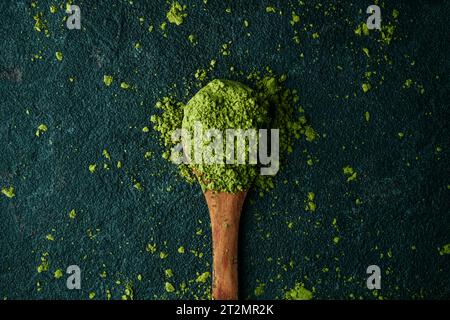 vista ad angolo elevato di alcuni tipi di tè in polvere matcha in un cucchiaio di legno posizionato su una superficie in pietra scura Foto Stock