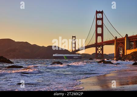 Transatlantico che passa sotto il Golden Gate Bridge al tramonto dalla spiaggia sabbiosa con onde Foto Stock