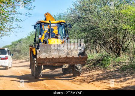 caricatore pesante che guida su una strada sterrata nella boccola che conduce al cantiere Foto Stock