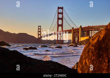 Luce dorata sul Golden Gate Bridge al tramonto con vista tra i massi della baia Foto Stock