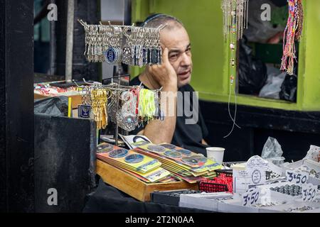 Tel Aviv, Israele - 17 agosto 2023: Venditore di souvenir e gioielli che si rilassa al mercato del Carmelo Shuk HaCarmel a Tel Aviv, Israele, un mercato popolare Foto Stock