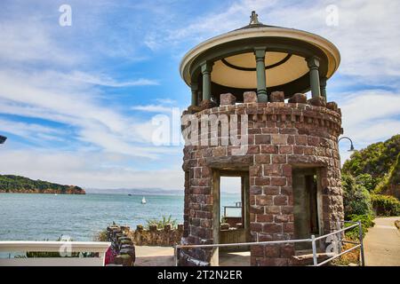 Torre in pietra marrone accanto al marciapiede con vista suggestiva della barca a vela bianca sull'acqua Foto Stock