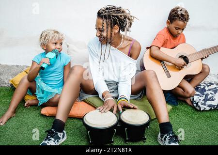 Felice famiglia africana che suona strumenti musicali sulla terrazza di casa - madre e bambini che si divertono all'aperto - rapporto di famiglia Foto Stock
