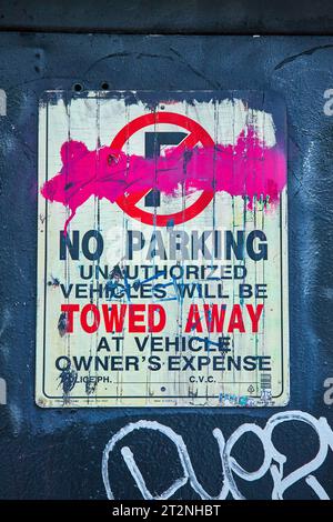 Graffiti rosa scuro sul cartello di DIVIETO DI PARCHEGGIO sulla parete con istruzioni dettagliate per il veicolo Foto Stock