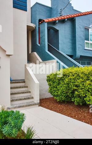 Marciapiede che conduce alle scale che salgono su una casa bianca accanto alla casa blu jean con tetto di tegole rosse Foto Stock