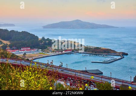 Tramonto arancione sulla baia di San Francisco con barche e moli in acqua sotto l'inizio del ponte Foto Stock