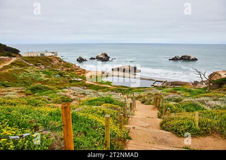 Ampia vista del sentiero sabbioso con scale che conducono all'oceano con struttura abbandonata e spiaggia Foto Stock