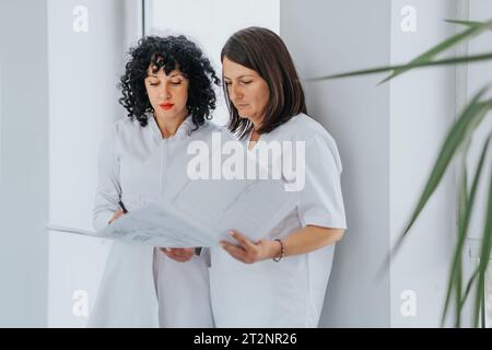 In un ambiente di lavoro sanitario, due professionisti discutono i risultati dei pazienti, collaborano sui risultati medici e lavorano insieme per fornire un'assistenza efficace. Foto Stock