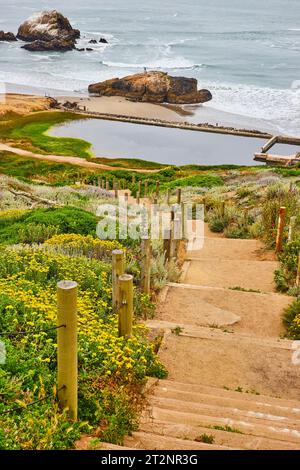 Sentiero sabbioso con scale che conducono all'oceano con struttura abbandonata e spiaggia Foto Stock