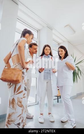 Gruppo di medici che consigliano una coppia sorridente in una clinica, discutendo risultati medici, opzioni di gravidanza, e soluzioni di trattamento di successo. Foto Stock