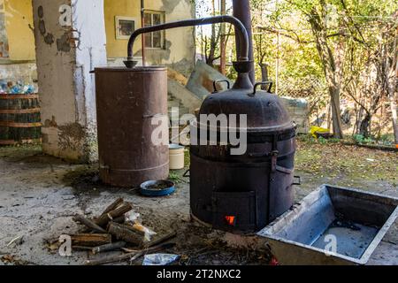 La pentola di distillazione, un elemento chiave nel processo di produzione di bevande alcoliche, si trova in un umile cortile rurale Foto Stock