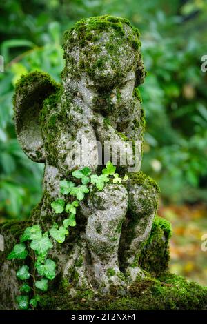 il muschio copriva un piccolo putto seduto stanco su una pietra in una tomba in un cimitero Foto Stock