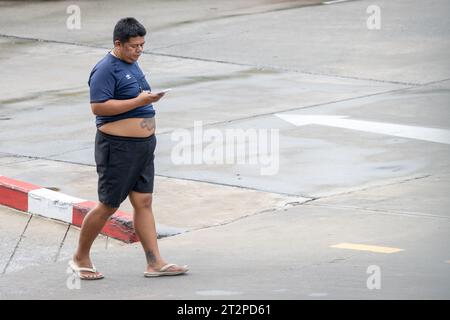 SAMUT PRAKAN, THAILANDIA, 12 giugno 2023, Un uomo cammina su una strada bagnata e guarda il suo cellulare Foto Stock