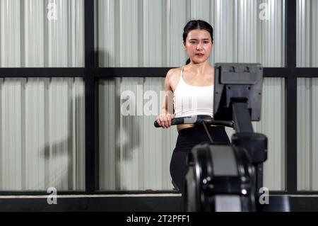 Concetto di salute e stile di vita attivo. Una donna atletica che indossa abbigliamento sportivo è impegnata in un'intensa sessione di allenamento su una vogatrice all'interno di un ben attrezzato Foto Stock