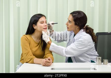 Un fornitore di assistenza sanitaria professionale sta eseguendo con precisione una procedura di diagnosi del naso su una paziente di sesso femminile in un ambiente clinico igienizzato. Loro una Foto Stock