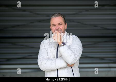 Uomo che indossa una giacca invernale bianca che sembra amichevole con la fotocamera, davanti a una parete in ferro ondulato Foto Stock