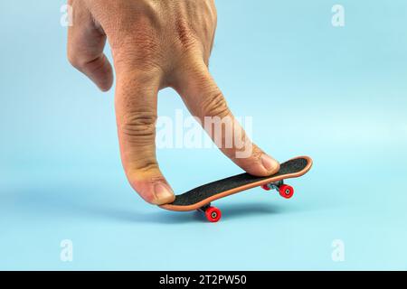 Skateboard piccola su sfondo a colori. Mano su un piccolo skate. Dita che giocano con la tastiera. Concetto di home Leisure. Spazio di copia Foto Stock