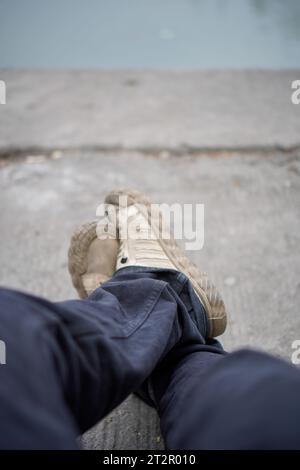 gambe lisce per rilassarsi dopo la routine. pantaloni neri e scarpe color crema su uno sfondo fluviale sfocato. Foto Stock