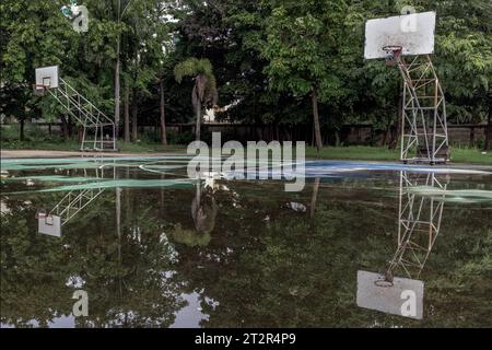 Due tabelloni da basket in legno con anelli in metallo e la rete bianca mostrano il loro riflesso sull'acqua piovana in tutto il vecchio basket Foto Stock