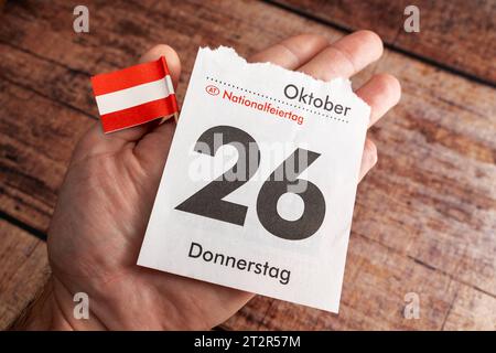 21 ottobre 2023: Mano che tiene una pagina del calendario con la data 26 ottobre, festa nazionale in Austria *** mano hält ein Kalenderblatt mit Datum 26 Oktober, Nationalfeiertag a Österreich Foto Stock