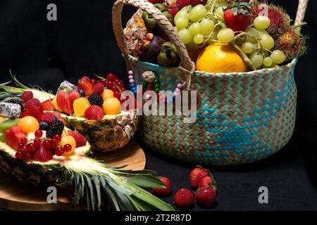 Composizione con frutta assortita in cestino di vimini isolato su sfondo nero Foto Stock