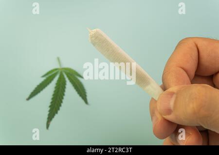 Un'articolazione di cannabis in mano di un uomo su sfondo blu da vicino. Concetto di utilizzo della pentola. Foto Stock