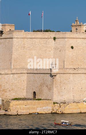 La dghajsa maltese (simile a una gondola) trasporta passeggeri tra la Valletta e Birgu a Malta con forte Sant'Angelo sullo sfondo. Foto Stock