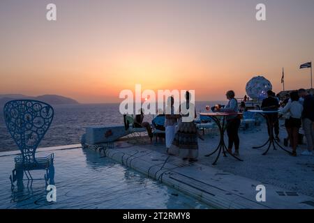 IOS, Grecia - 11 settembre 2023: I giovani si riuniscono intorno alla piscina in un Lounge bar per guardare il tramonto a iOS cicladi Grecia Foto Stock