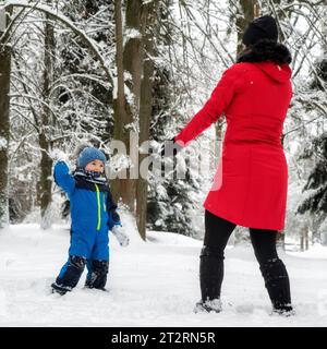 Madre con bambino che gioca nella foresta invernale innevata. Foto Stock
