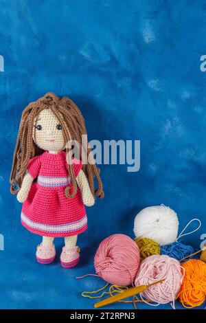 Bambola Amigurumi realizzata a mano su sfondo blu con i filati utilizzati per la sua elaborazione Foto Stock