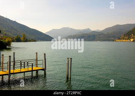 Molo sul lungomare in una soleggiata giornata estiva e con vista sul Lago di Lugano e sulle montagne di Morcote, Ticino, Svizzera Foto Stock