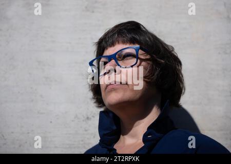 Colpo alla testa su una donna elegante con occhiali da vista e appoggiarsi su un muro di cemento in una giornata di sole in Svizzera Foto Stock