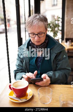 Donna anziana, Best Ager, seduta in un bar, bevendo caffè, digitando smartphone, cellulare, Parigi, Francia Foto Stock