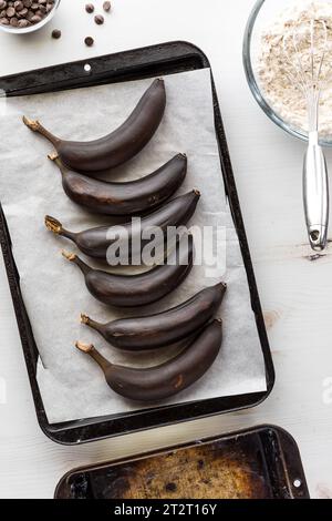 Banane arrostite su una teglia da forno rivestita di carta pergamena per preparare il pane alla banana. Foto Stock