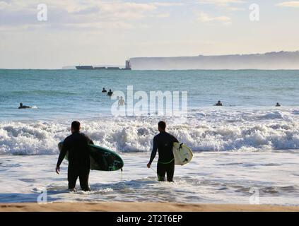 Surfisti che camminano in mare con una nave da carico distante che lascia il porto di Santander in una soleggiata mattinata di ottobre Sardinero Santander Cantabria Spagna Foto Stock