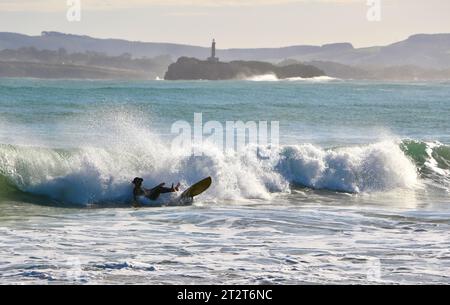 Un surfista con l'isola di Mouro all'ingresso della baia con forti onde in una soleggiata mattinata autunnale Sardinero Santander Cantabria Spagna Foto Stock