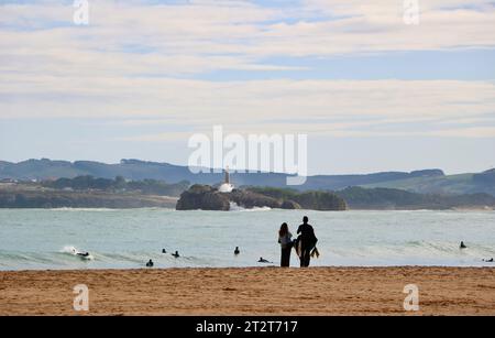 Una donna in piedi sulla spiaggia che parla con i surfisti con l'isola di Mouro in lontananza in una soleggiata mattinata autunnale Sardinero Santander Cantabria Spagna Foto Stock