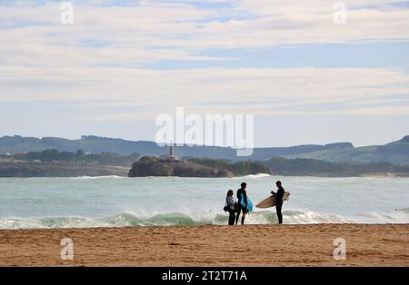 Una donna in piedi sulla spiaggia che parla con i surfisti con l'isola di Mouro in lontananza in una soleggiata mattinata autunnale Sardinero Santander Cantabria Spagna Foto Stock