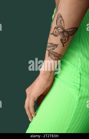 Giovane donna con braccio tatuato su sfondo verde, primo piano Foto Stock