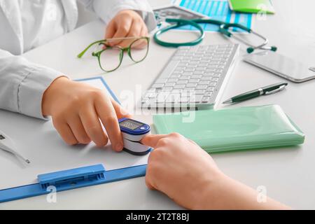 Medico femminile che prende polso da paziente a scrivania medica bianca, primo piano Foto Stock