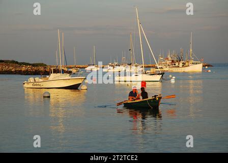 Un adulto si reca in barca su un gommone su un calmo porto d'acqua in un giorno d'estate Foto Stock