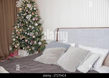 Regali di Natale avvolti su un comodo letto accanto all'albero di Natale. Lussuosa, decorata con ghirlande e palle, regali rosa, appartamento Foto Stock