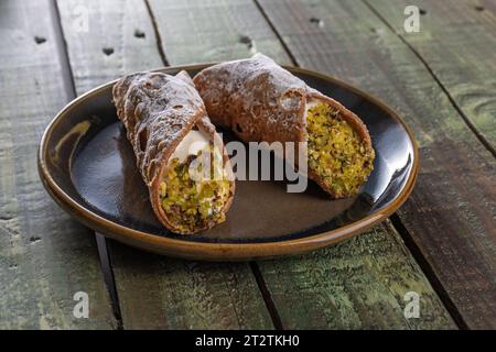 Primo piano dei tradizionali cannoli siciliani ripieni di pistacchio cremoso su un rustico tavolo in legno. Foto Stock