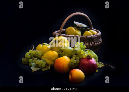 una natura morta con quinces, uva, pere e mele con un cesto e fondo nero Foto Stock