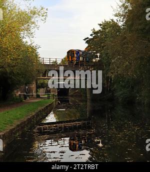 Una DMU dei treni del Nord si riflette nelle acque coperte di foglie autunnali del canale di Leeds e Liverpool sopra il volo delle chiuse di Wigan. Foto Stock