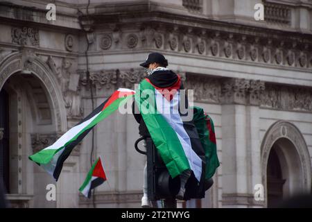 Londra, Regno Unito. 21 ottobre 2023. Un manifestante sale al semaforo con bandiere palestinesi durante la manifestazione a Whitehall. Decine di migliaia di persone hanno marciato nel centro di Londra in solidarietà con la Palestina mentre la guerra Israele-Hamas si intensifica. Credito: SOPA Images Limited/Alamy Live News Foto Stock