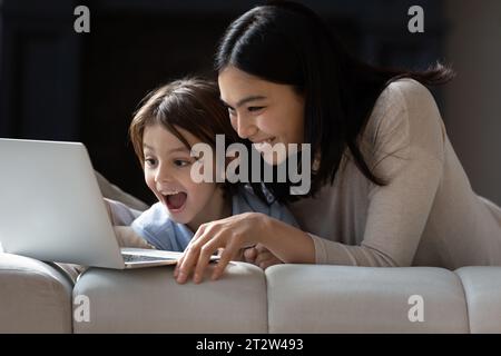 Felicissimo ragazzo dei 7 anni con madre asiatica che guarda lo schermo del notebook Foto Stock