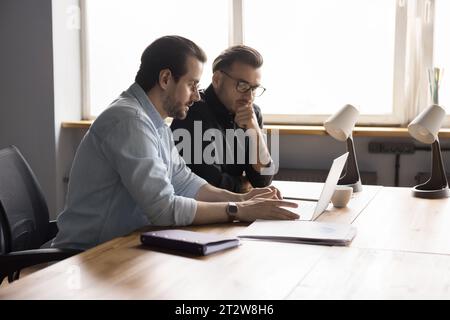 Due colleghi maschi che lavorano in un ufficio moderno utilizzando un computer portatile Foto Stock